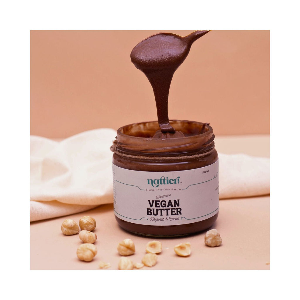 Jar of vegan butter with a spoon full of butter surrounded by nuts on a beige background