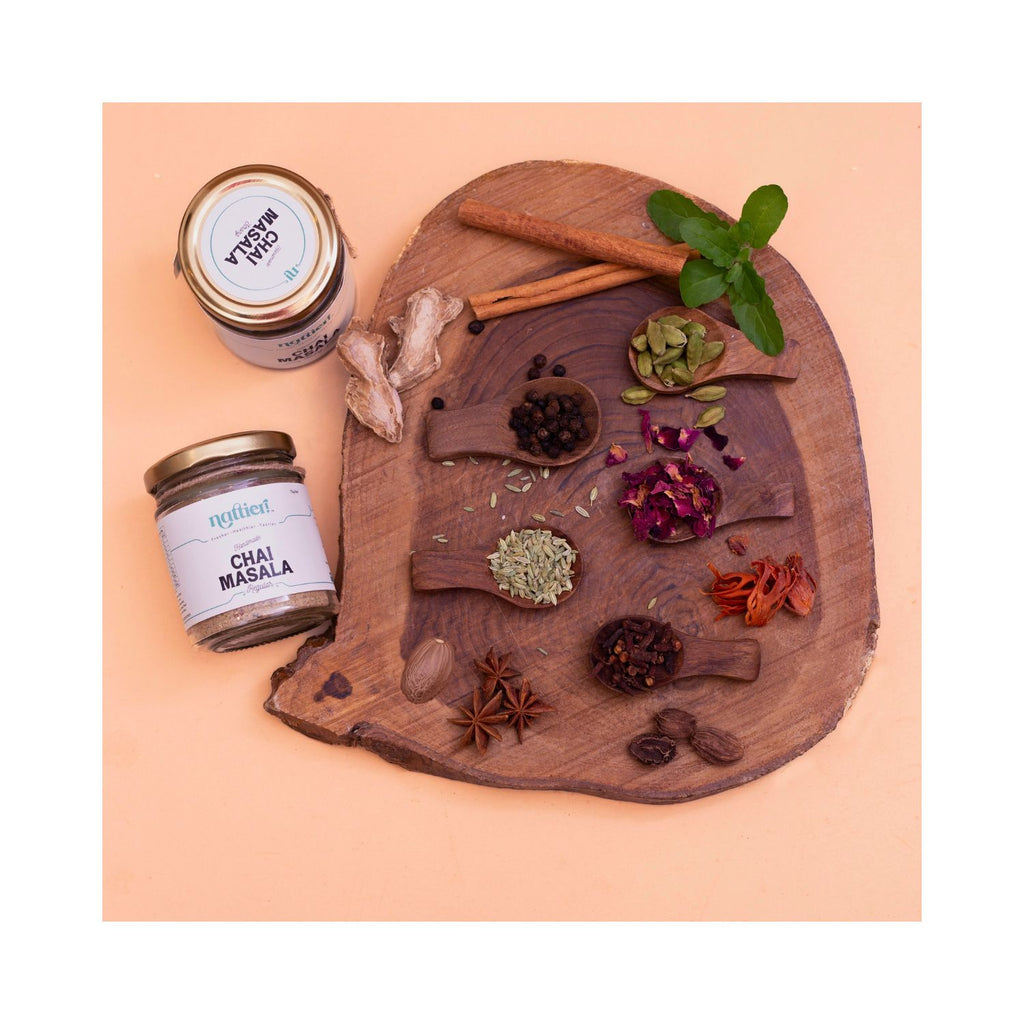 Spices and a jar of 'Chai Masala' on a wooden board with a peach background