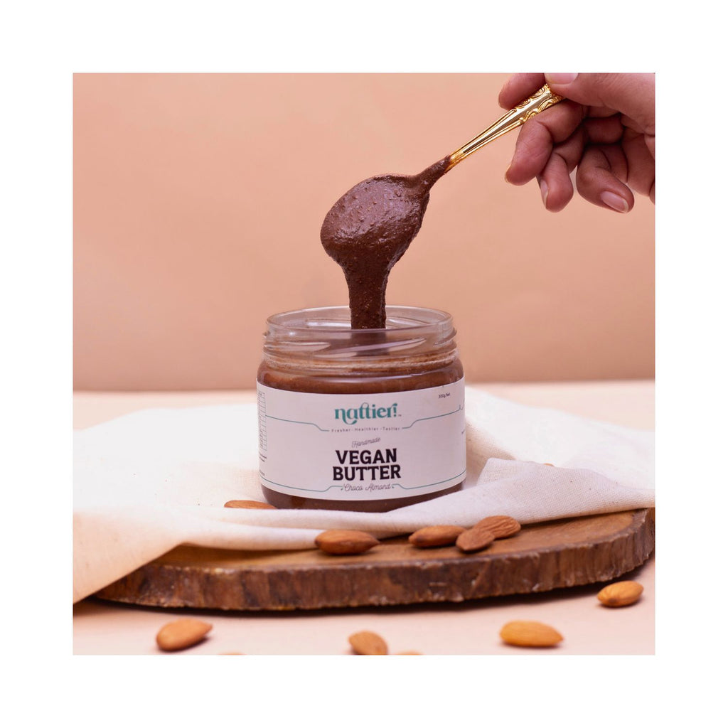 Jar of vegan butter with a spoonful being lifted, surrounded by almonds on a wooden board.