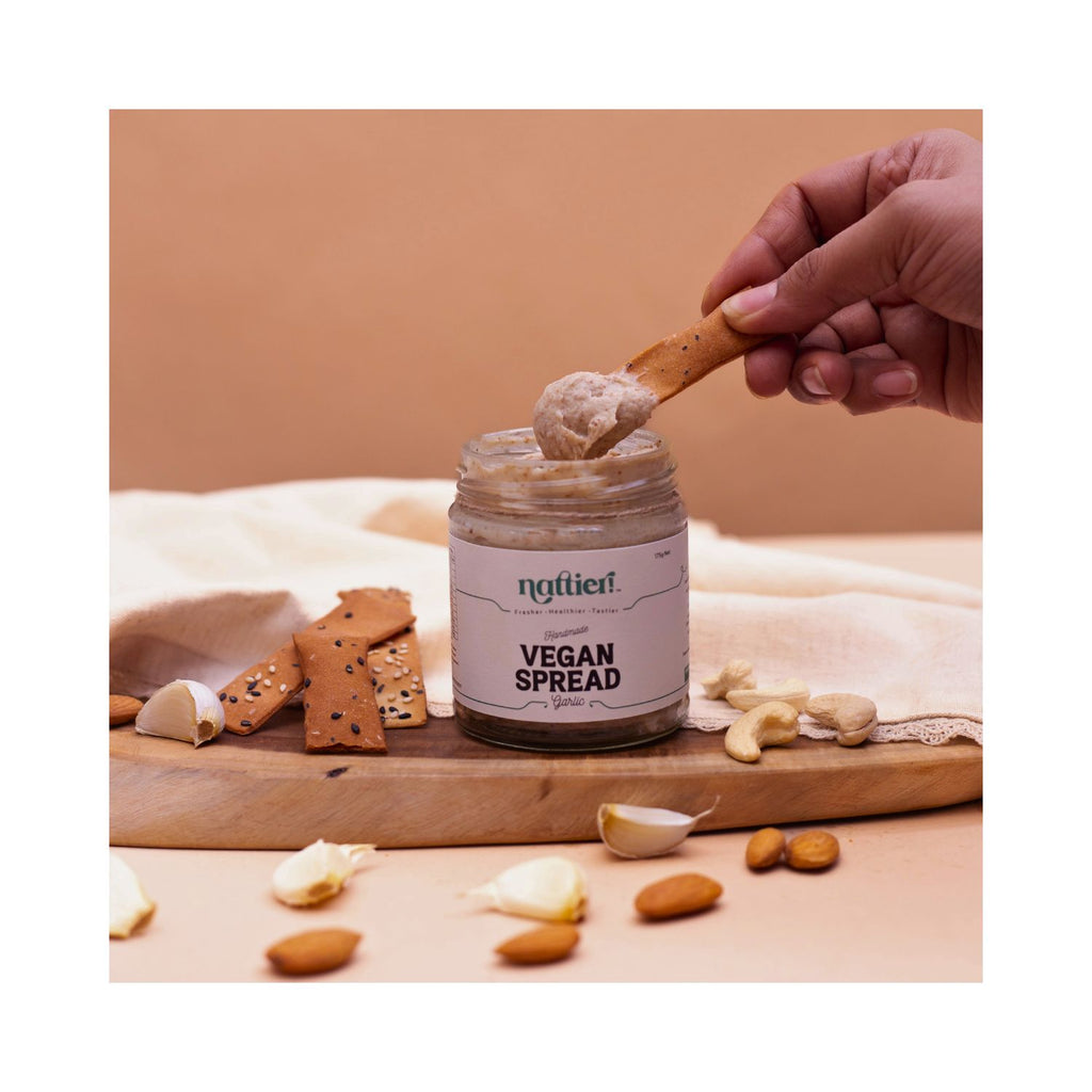 Open jar of vegan spread with a cracker dipping into it placed on a wooden board on a brown and white background