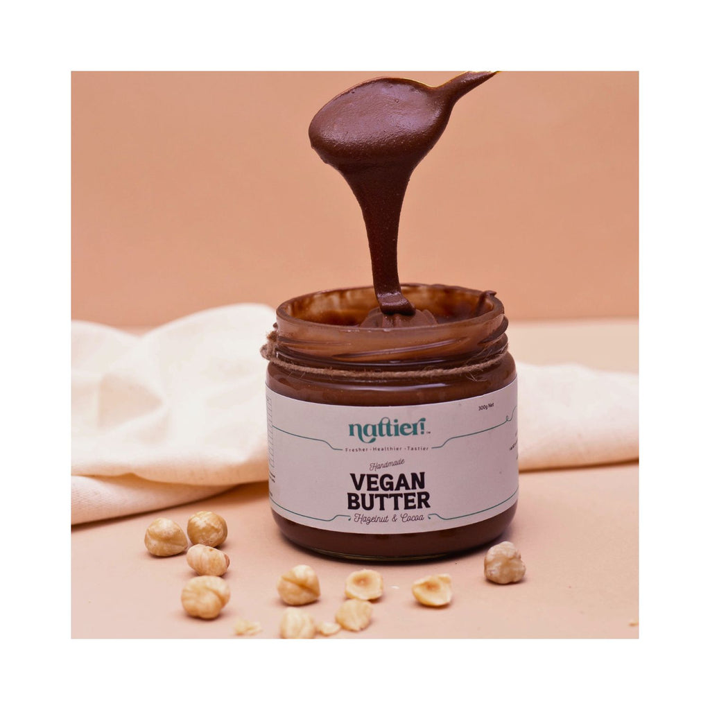 Jar of vegan butter with a spoonful being poured, surrounded by nuts on a beige background.