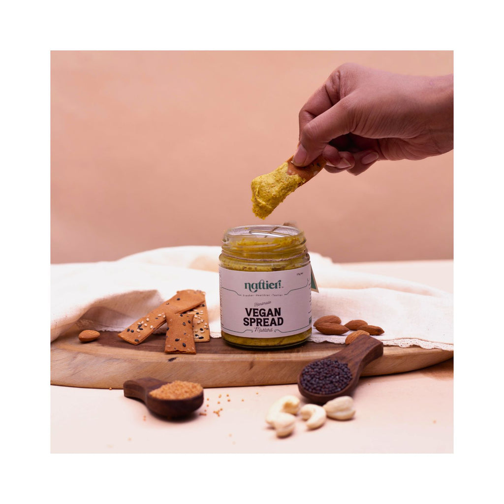 Person dipping a cracker into a jar of vegan mustard spread with a brown and white background