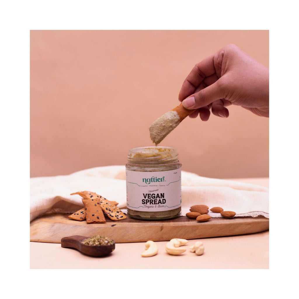 Persons hand dipping cracker in jar on wooden board with brown and white background